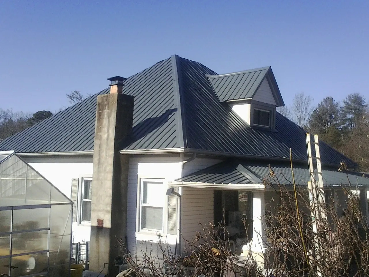 Dark blue standing seam metal roof on a white farmhouse with dormer — Slate & Tile Roof Repair by Roofing Brothers in Wessington Springs