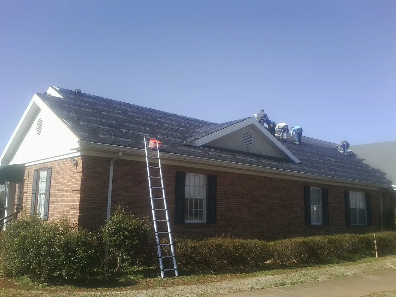 Crew tearing shingles off a brick ranch roof with a ladder set — Metal Roof Repair work by our crew in Wessington Springs