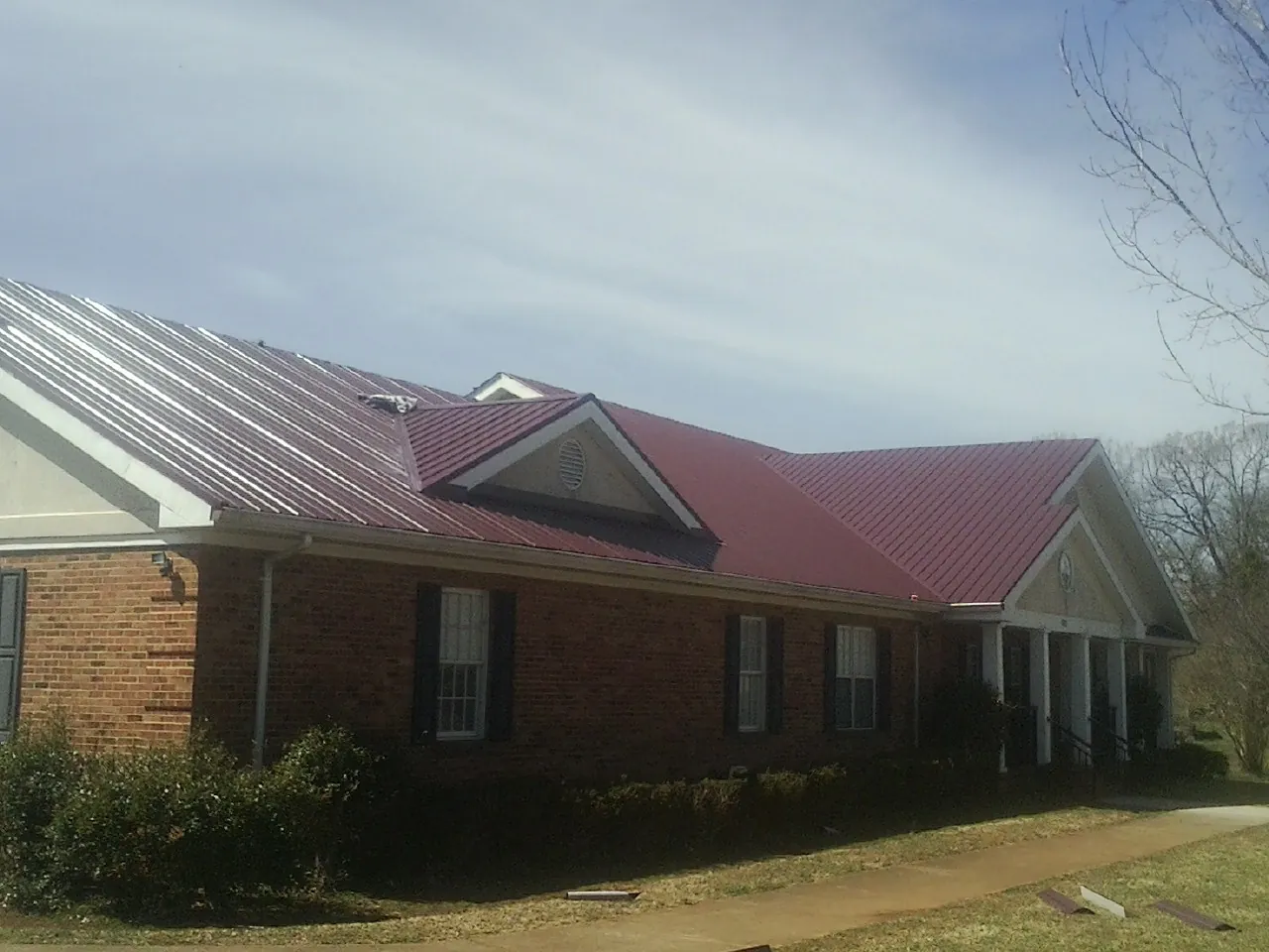 Red metal roof with gabled entries on a long brick building, from a Hail Damage Roof Repair job in Wessington Springs