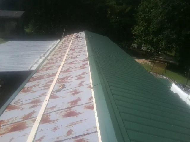 Old rusted panels beside newly installed green metal roofing — Wind Damage Roof Repair by Roofing Brothers in Wessington Springs