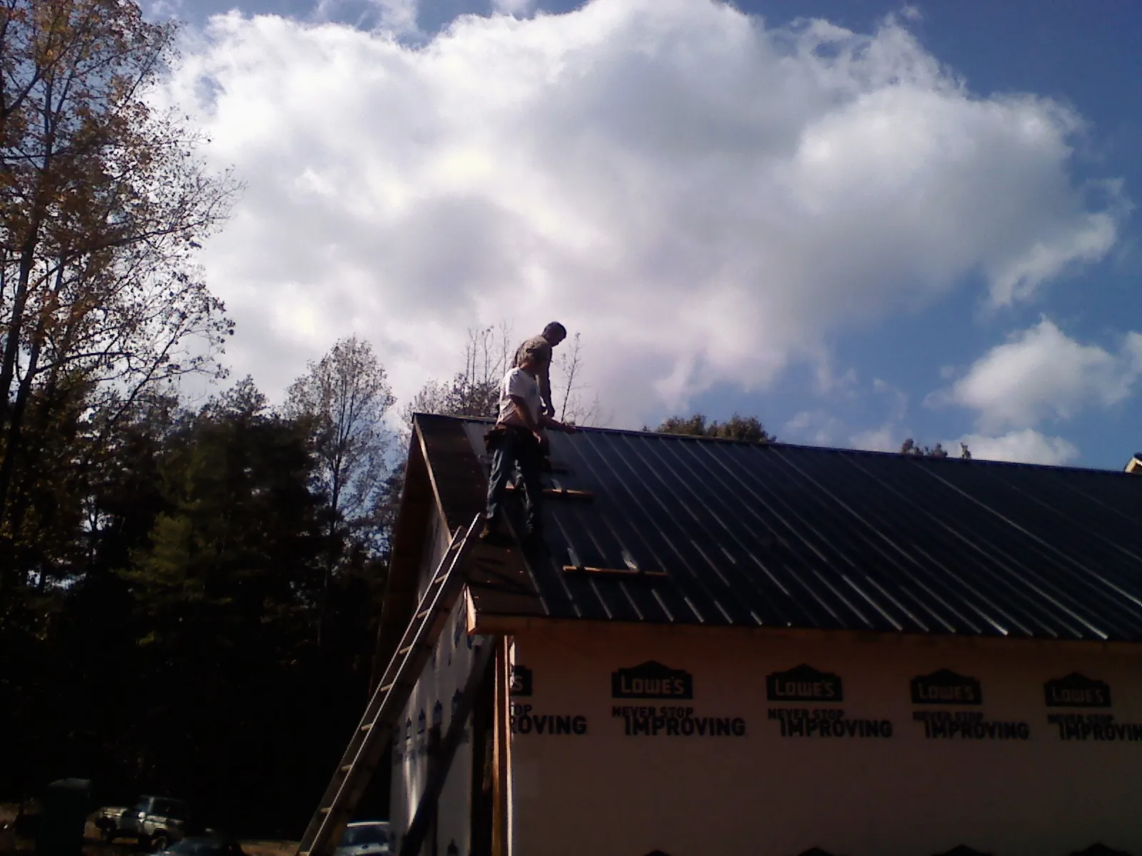 Roofer fastening dark metal panels high against a cloudy sky, from a Roof Inspection job in Wessington Springs