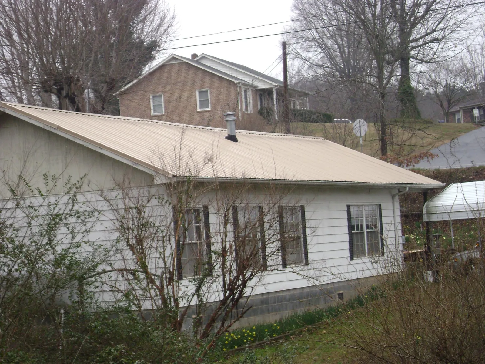 Tan metal roof on a white sided house set into a hillside — Commercial Roofing by Roofing Brothers in Wessington Springs